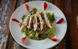 Grilled chicken salad on a white plate, garnished with strawberry slices