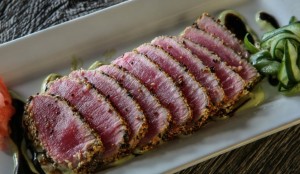 Sliced seared tuna on a rectangular plate with greens and garnish