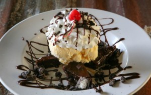 Chocolate dessert topped with whipped cream, ice cream, and a cherry on a plate