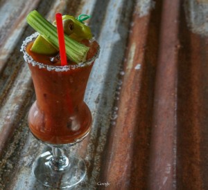 A Bloody Mary cocktail with celery, olives, and a red straw in a salt-rimmed glass